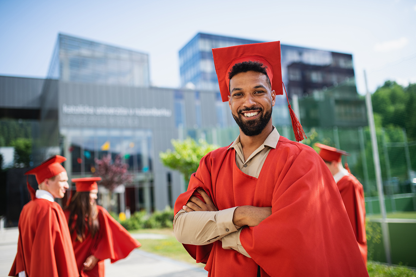 Graduate in cap and gown faces camera with modern buildings in background